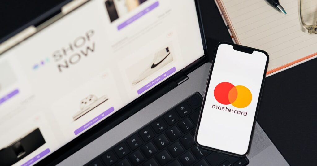 Laptop showing a webshop with Add to cart buttons and a phone showing a payment card logo, seen from above