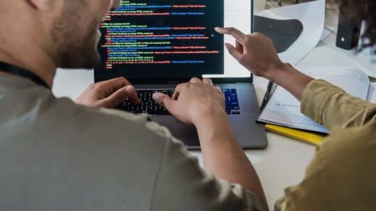 Ontwikkelaar die aan code werkt op een laptop, bij een blog over QA als bottleneck