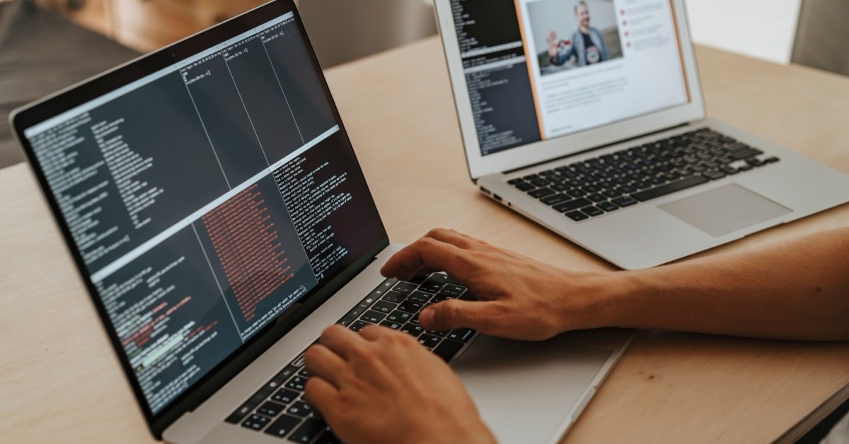 Handen typen op een laptop met terminalvensters vol testresultaten, met een tweede laptop op de achtergrond