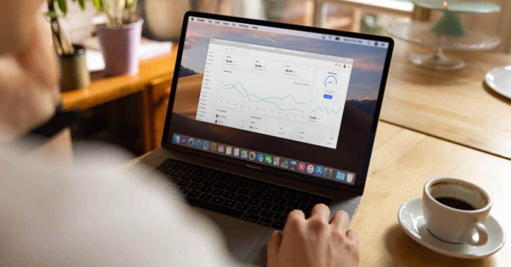 Person working on a laptop showing a sales dashboard with charts, with a cup of coffee on the table